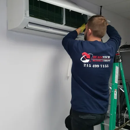 QualiTech technician servicing a ductless mini-split indoor unit on a ladder